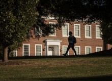 A woman with a backpack walks across a college campus.