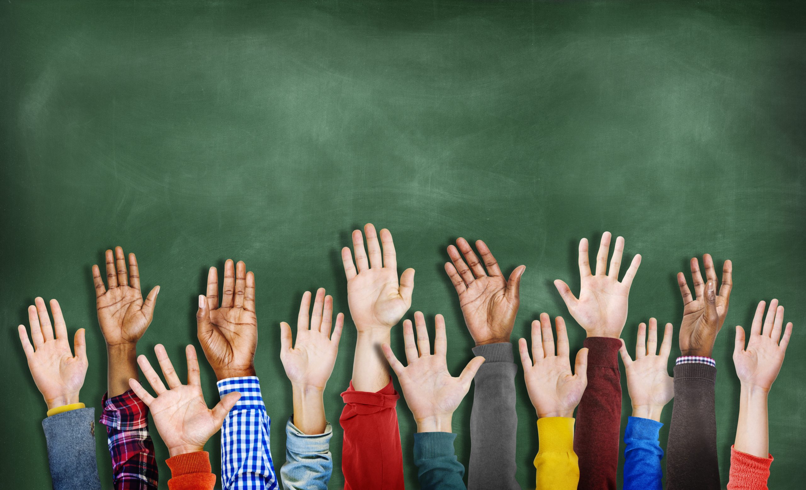 Raised hands of children in front of a chalkboard.