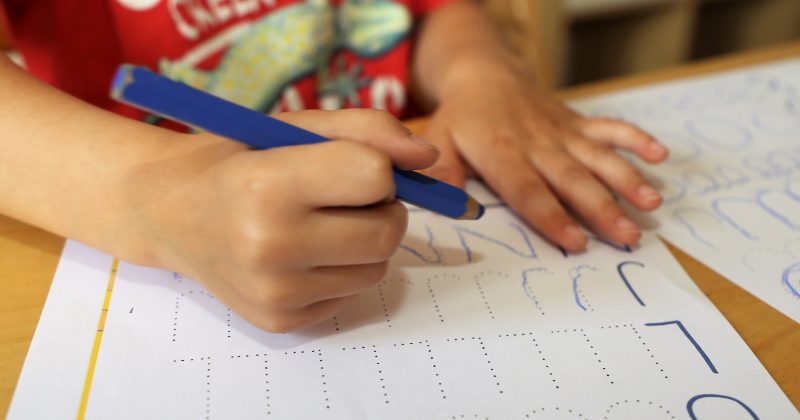 A closeup of a child's hands as he practices writing letters.